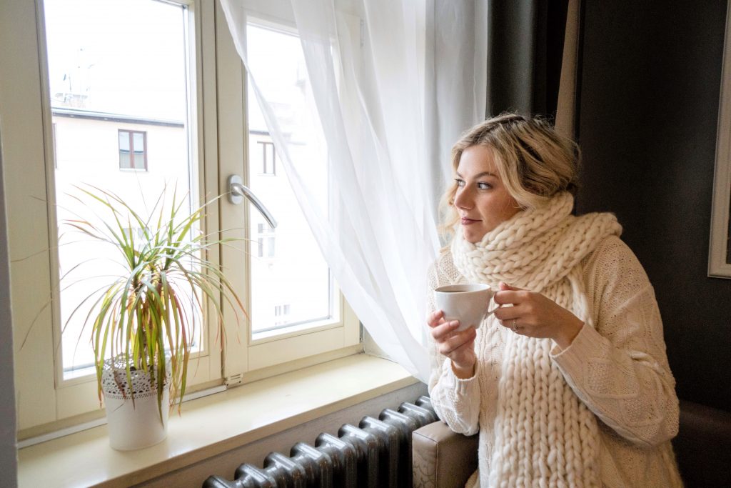 girl wearing chunky scarf looking out window with tea