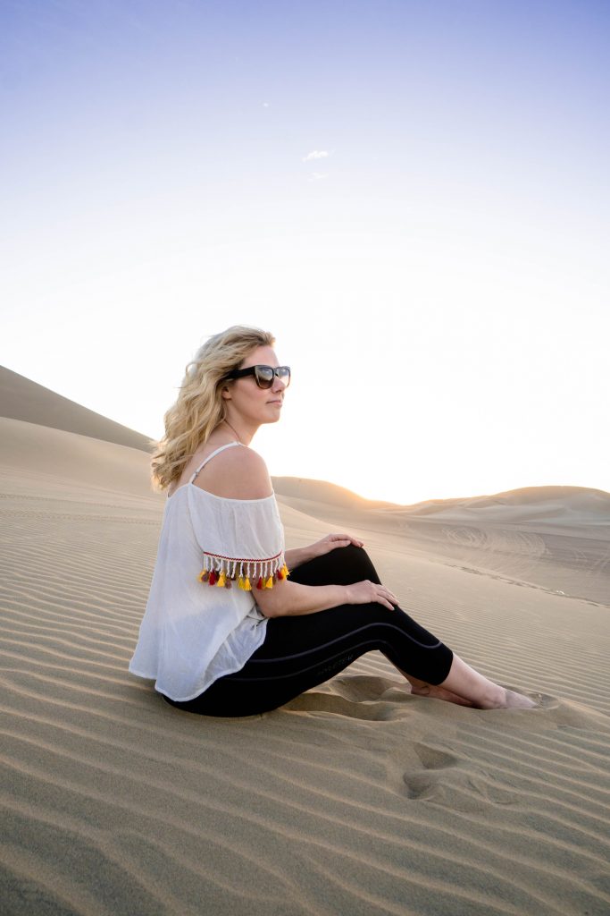 traveling with HYLETE; girl sitting on sand dunes Huacachina Peru