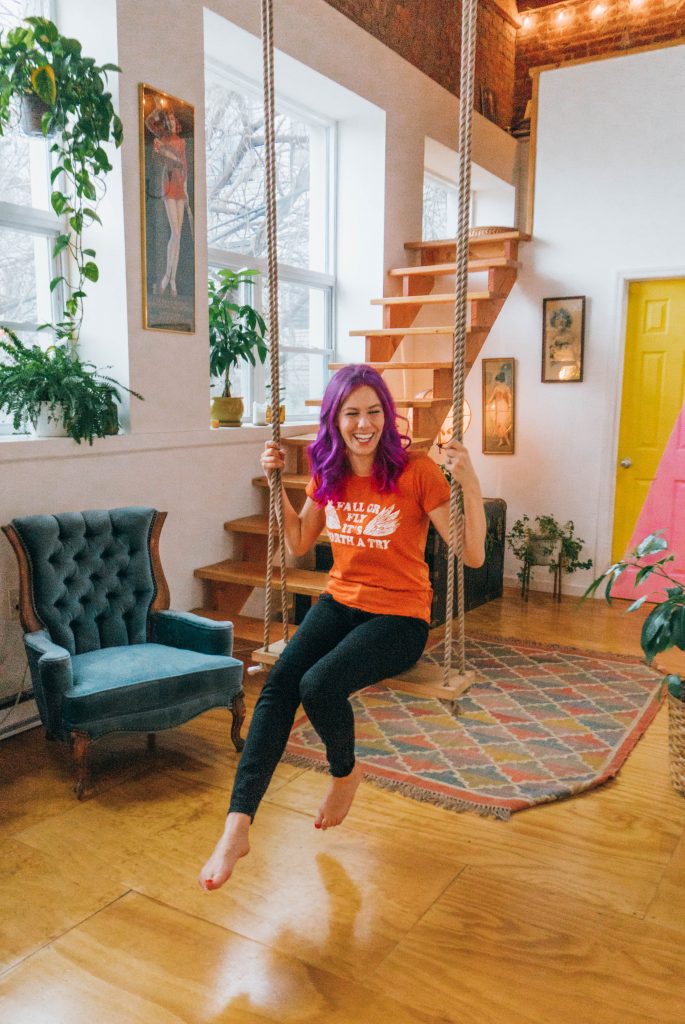 Staying at The Funky Loft in Brooklyn, New York; girl with purple hair on indoor swing in retro apartment